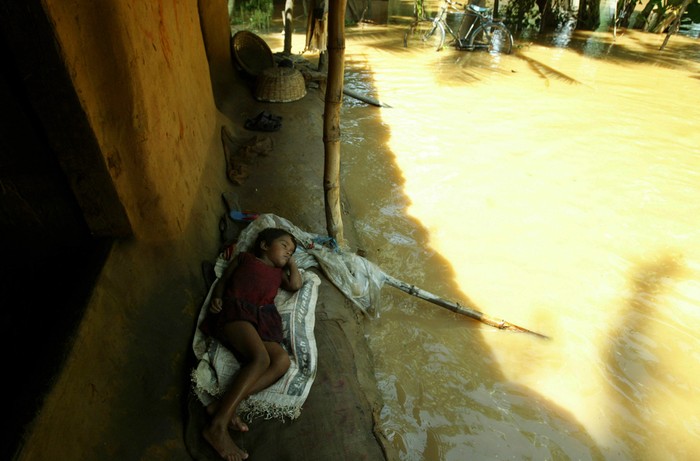 Một em bé đang nằm ngủ trên thềm nhà khi nước lụt đang vây quanh ở làng Pahanga.
